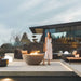 Woman Standing Next To a Fire Pit In Front Of The Arya Outdoor Modular Sectional Sofa In Acadia Color