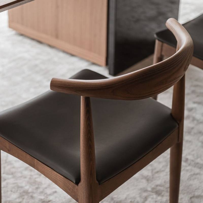 Close Up View of The Elbow Chair in Trento Jet Black and Wood Finishes at a Dining Table