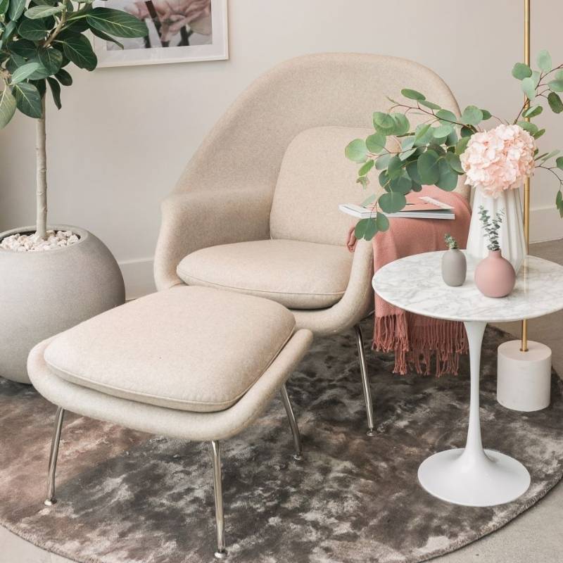 Angled View of The Womb Chair and Ottoman in Pearl Fabric Next to a Side Table