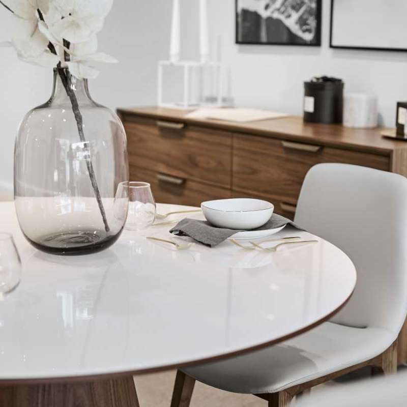 Close Up View of The Winston Dining Table 48 Inch With High Gloss White Lacquer Surface and Walnut Veneer Finish With Cabinet in the Background